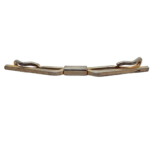 Front view of the 1930's vintage collar clip. It is darkened gold tone in color and has a thin etched line pattern on the front of the bars. There is a chip in the gold tone plating on the right when viewed closely and some rub wear can be seen on the back where the base metal shows through.