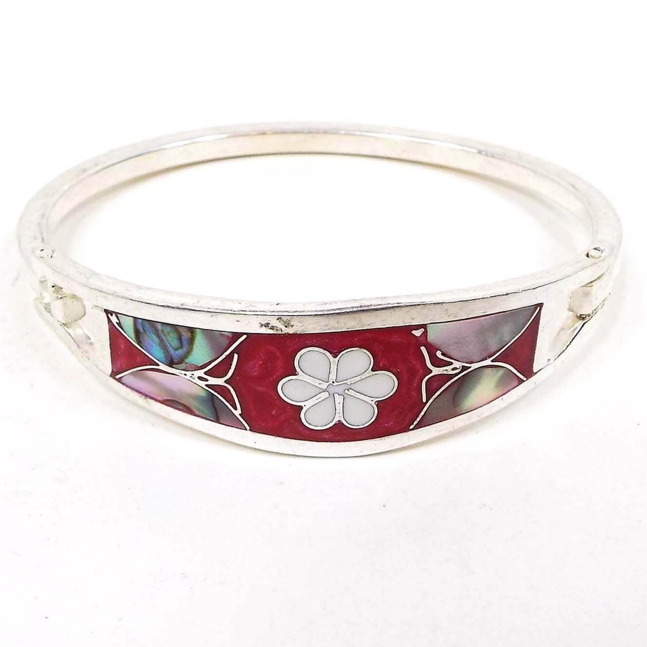 Angled front view of the Mexican butterfly and flower hinged bangle bracelet. The metal is silver tone in color. The front has pearly dark pink enamel with a white enamel flower in the middle and an abalone shell butterfly on each side. 