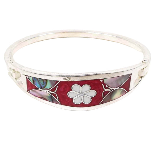 Angled front view of the Mexican butterfly and flower hinged bangle bracelet. The metal is silver tone in color. The front has pearly dark pink enamel with a white enamel flower in the middle and an abalone shell butterfly on each side. 