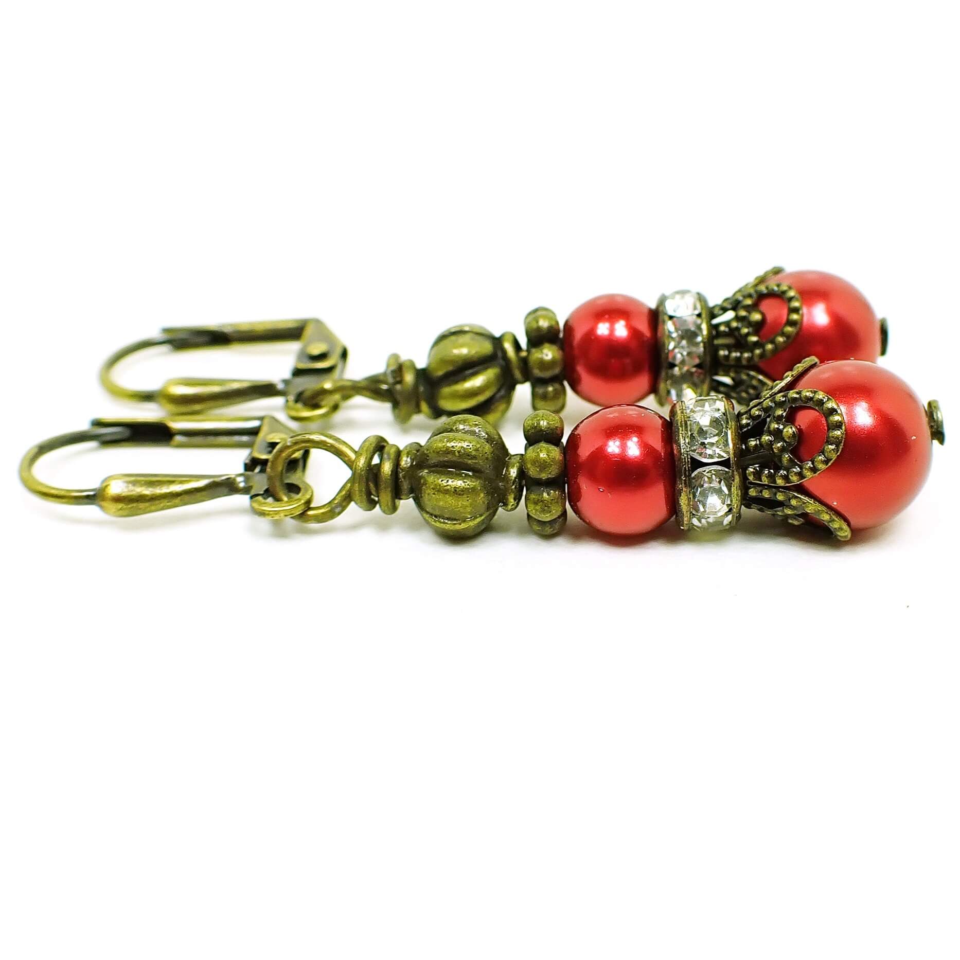 Side view of the handmade glass beaded earrings with rhinestones. The metal is antiqued brass in color. The earrings are beaded with a round metallic red coated glass bead, a rhinestone spacer bead, and then another larger round metallic red glass bead. 