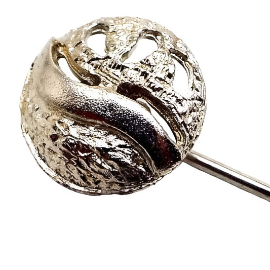 Enlarged view of the top of the retro vintage two tone stick pin. The pin is silver tone in color. The top part has a circle with cut out areas on the right and textured gold tone color metal.