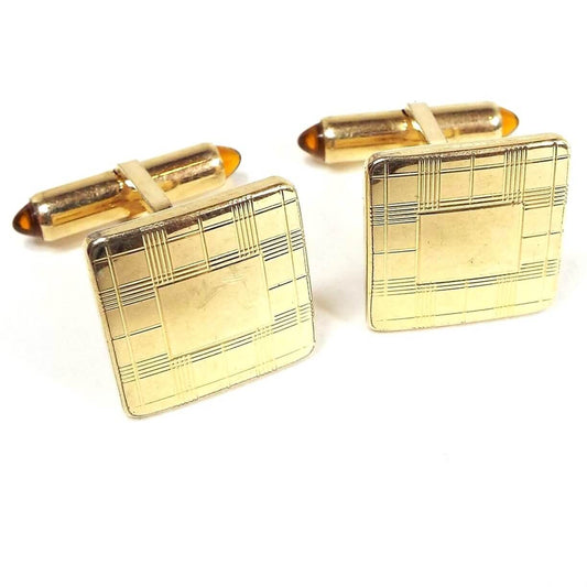 Front view of the Mid Century vintage Krementz cufflinks. They are square and gold tone in color with a lightly etched plaid like pattern on the front. The backs have domed orange lucite caps on each side of the levers.