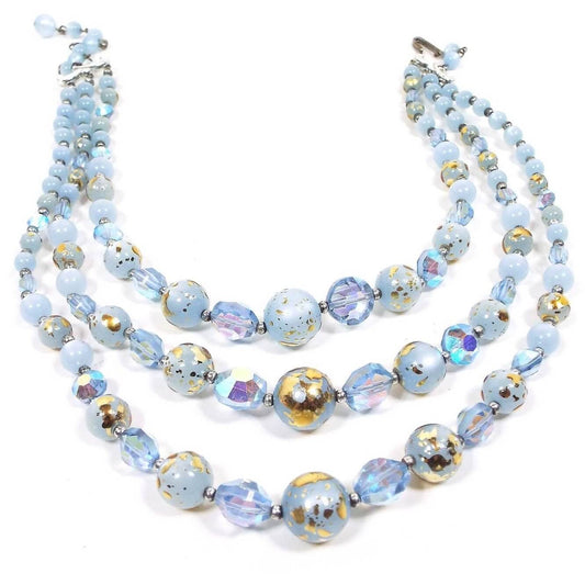 Front view of the Mid Century vintage multi strand necklace. There are three strands of light blue beads. There are round moonglow lucite and round lucite beads with metallic gold color splatter paint on them. In between here and there are AB blue crystal beads in a faceted sauce shape. The end clasp and other metal parts are silver tone in color.