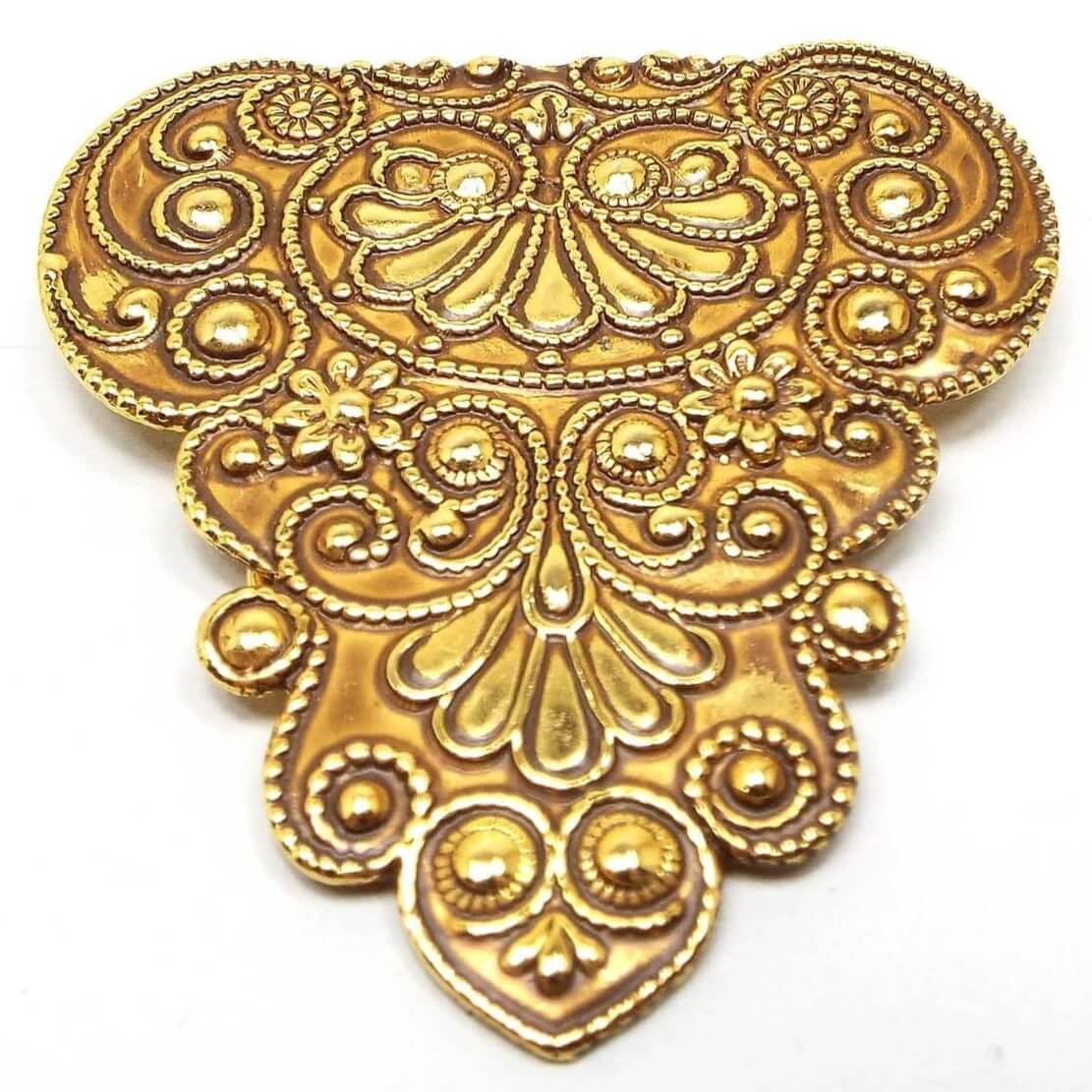 Front view of the retro vintage scarf clip. It is large in size and tapers down to the end with curves and swirls in the patter. There are also some flower designs in the stamped brass pattern.