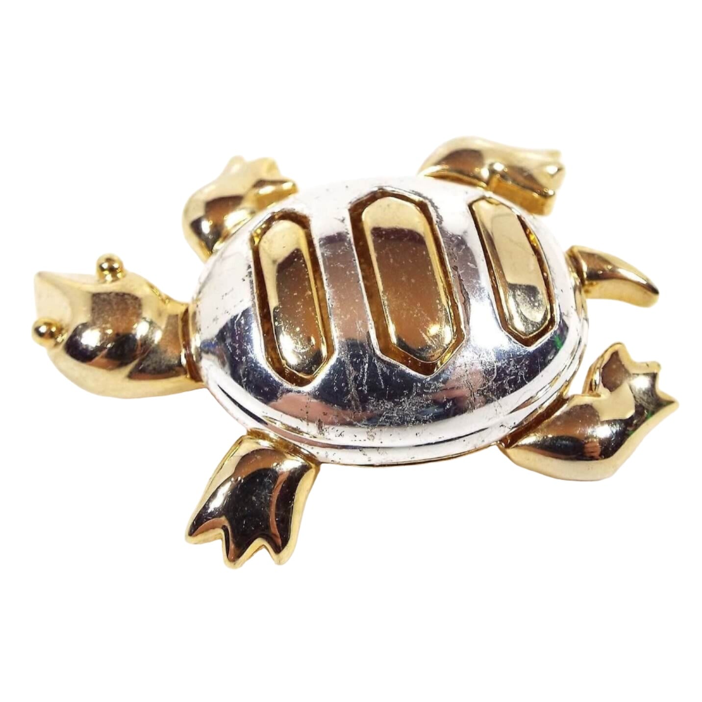 Top view of the Allison Reed retro vintage turtle brooch pin. The turtle appears to be on the move with his legs bent and his head turned to the right. His head, legs, tail, and stripes on top are gold tone in color and his shell is silver tone in color.