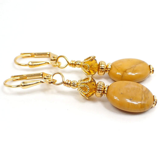 Side view of the handmade gemstone earrings. The metal is gold plated in color. There are faceted glass crystal beads at the top in a citrine orange color. The bottom jasper beads are oval shaped and have shades of mustard yellow, brown, and hints of orange.