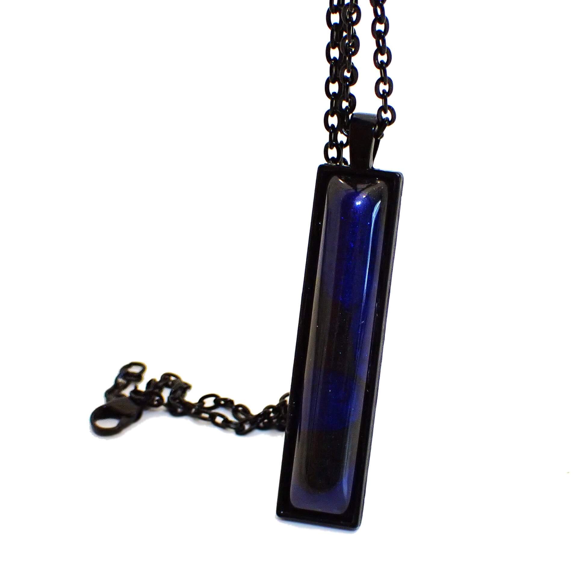 Enlarged front view of the handmade resin Goth pendant necklace. The metal is black coated. There is a long rectangle bar pendant at the bottom. The bar pendant has a handmade resin cab with marbled pearly black and deep blue colors.