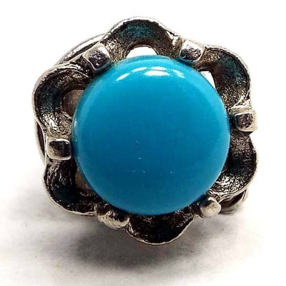 Enlarged view of the retro vintage faux turquoise tie tack. It has a silver tone color scalloped edge flower like design all the way around a round glass imitation turquoise cab. The cab is blue in color.
