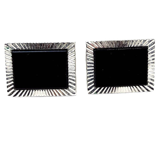 Front view of the Mid Century vintage cufflinks. The metal is silver tone in color. The fronts have rectangle black glass cabs surrounded by line textured silver tone settings.