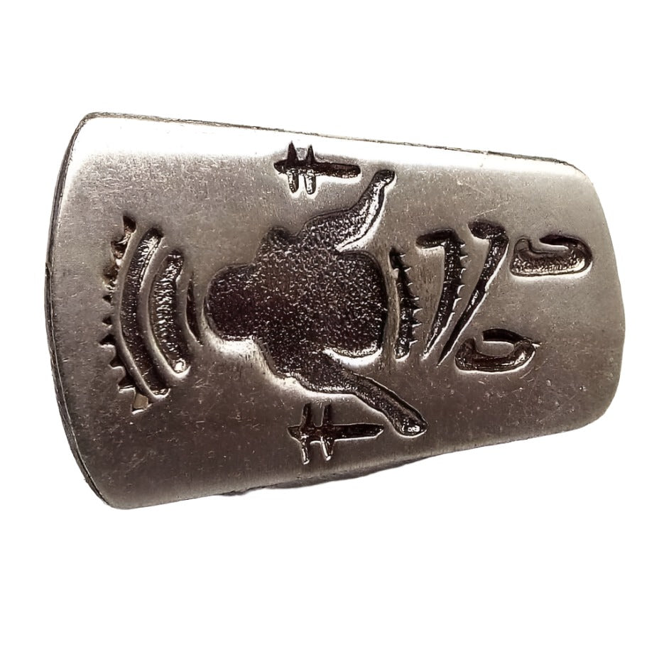 Front view of the retro vintage Kachina tie tack. It is silver tone in color and has an elongated shape. There front has a Southwestern style Kachina stamped on it.