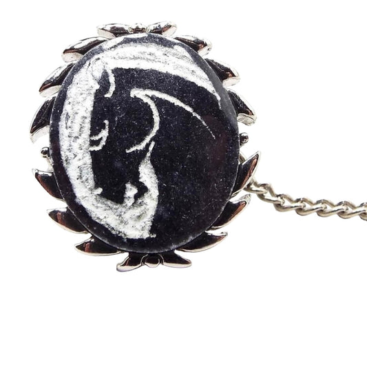 Enlarged front view of the retro vintage Swank carved stone tie tack. The metal is silver tone in color and has a leaf like curved design around the edge. The stone cab is black with white showing what's been carved away and has a horse head cameo.