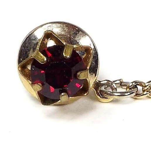 Enlarged front view of the 1950's Mid Century vintage rhinestone tie tack. The tie tack has an antiqued brass open star shape with a red rhinestone in the middle.. The clutch and chain are gold tone in color.