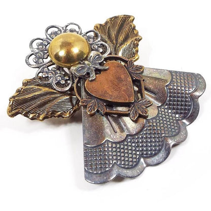 Angled front view of the retro vintage Kat's Creations brooch pendant. It is shaped like an angel with various pieces of stamped metals in different metal types and colors. 