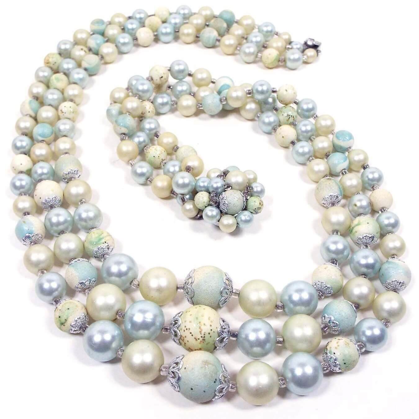 Top view of the Mid Century vintage Japan pastel beaded multi strand necklace. It has three rows of round plastic beads in light blue and yellow, along with some faux pearls in off white. There is a beaded box clasp at the end. 