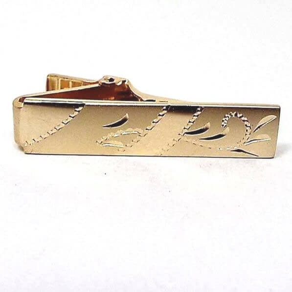 Front view of the Mid Century Vintage Anson etched tie clip. The metal is gold tone in color. There is a diagonal etched line design in three places with etched style leaves in between.