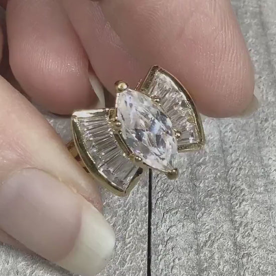 Video of the retro vintage rhinestone cocktail ring. The metal is gold tone plated in color. There is a large marquis rhinestone in the middle. Each side has a flared design with trapezoid shaped rhinestones. The video is showing the rhinestones sparkling.