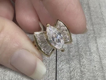 Video of the retro vintage rhinestone cocktail ring. The metal is gold tone plated in color. There is a large marquis rhinestone in the middle. Each side has a flared design with trapezoid shaped rhinestones. The video is showing the rhinestones sparkling.