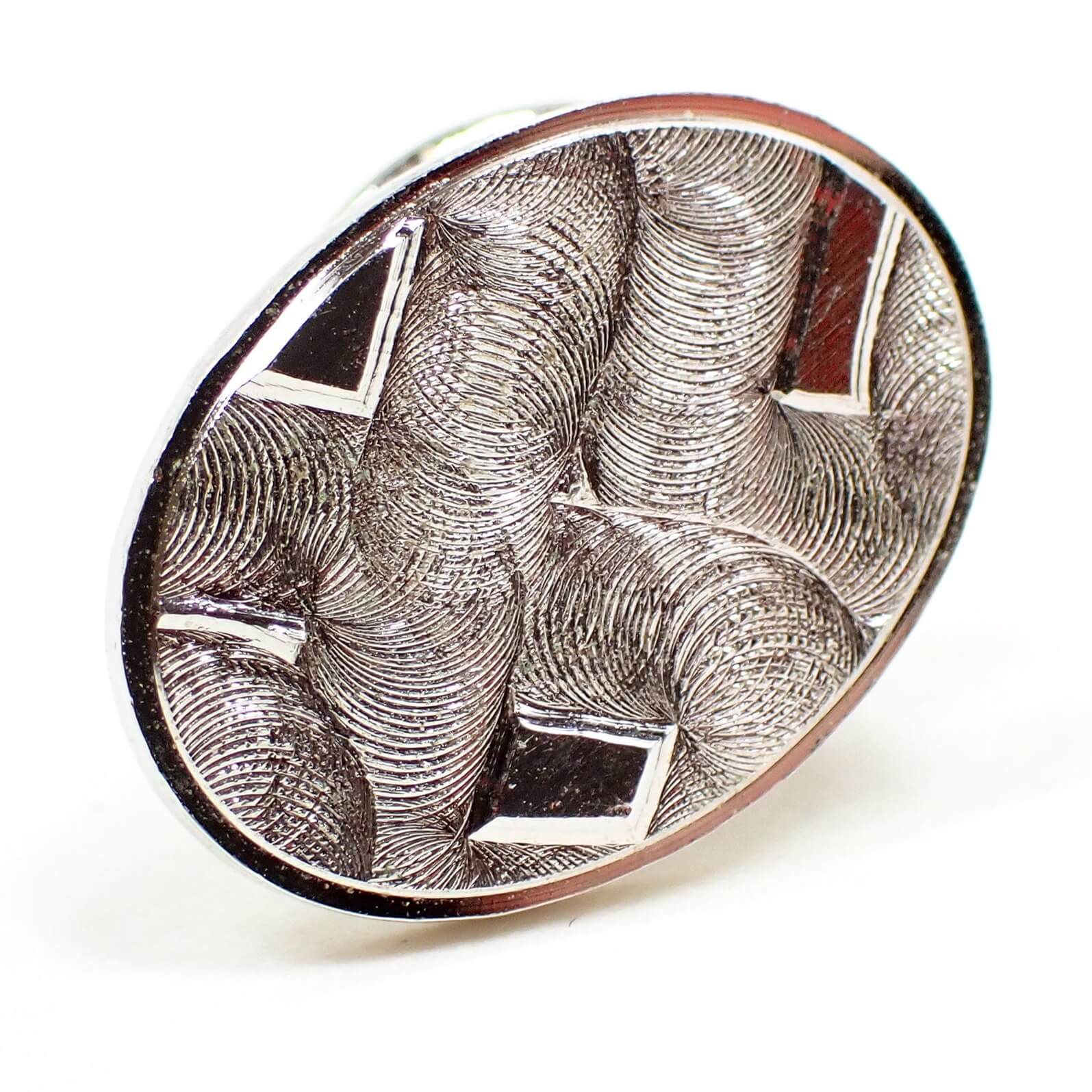 Enlarged front view of the retro vintage tie tack. It is oval in shape with a textured matte silver tone plated front. 