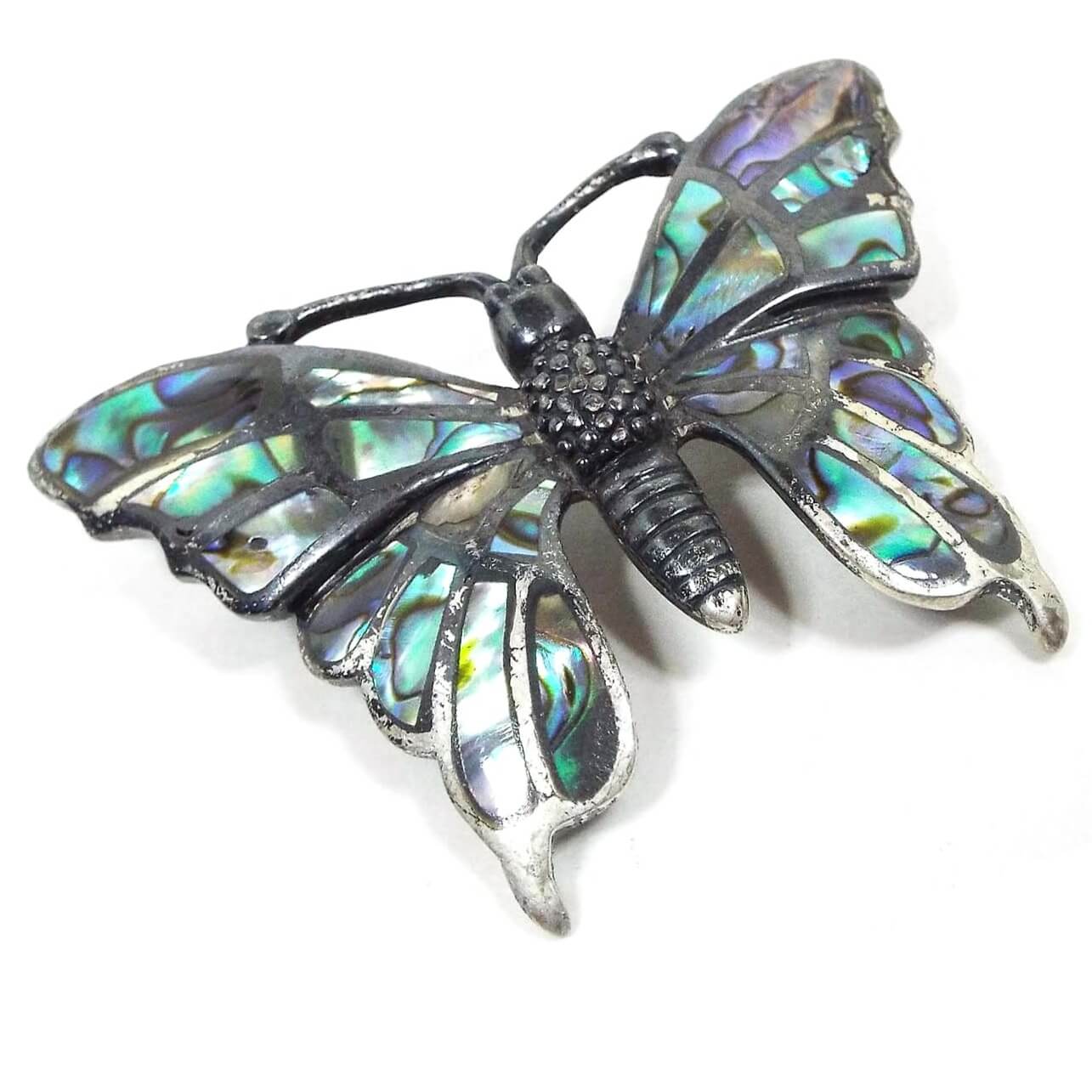 Front view of the retro vintage Southwestern Boho butterfly brooch pin. The sterling silver is very darkened in color to a really dark gray and black in some areas. The brooch is shaped like a butterfly with a textured body. The wings have areas on inlaid abalone shell that have various flashes of color as you move around in the light.