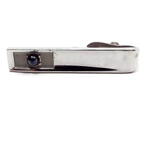 Front view of the retro vintage faux pearl tie clip. The metal is silver tone in color. At the end is a recessed rectangle with matte metal. In the middle of that is a dark gray glass faux pearl.
