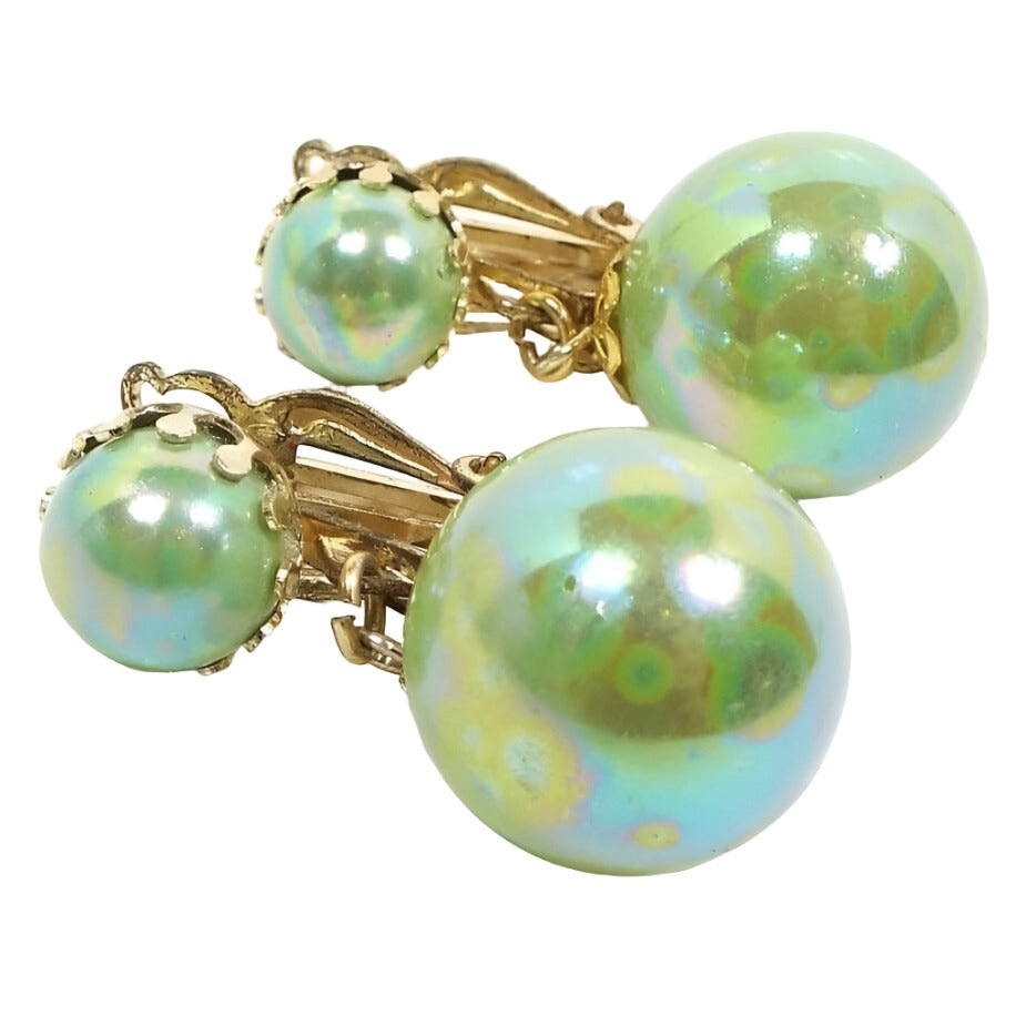 Front view of the Mid Century vintage clip on earrings from Japan. The metal is gold tone in color. They have pearly AB light green round beads on top and a larger drop bead at the bottom. 