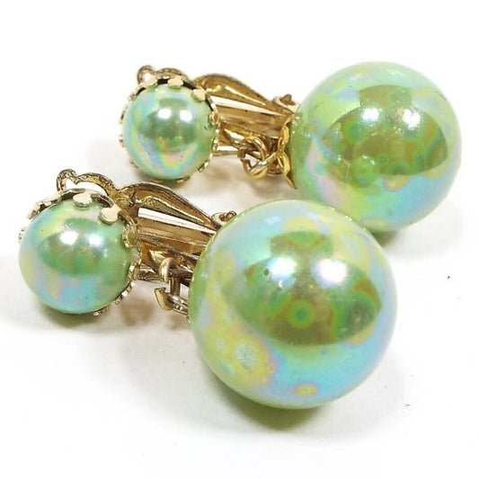 Front view of the Mid Century vintage clip on earrings from Japan. The metal is gold tone in color. They have pearly AB light green round beads on top and a larger drop bead at the bottom. 