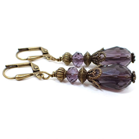 Side view of the handmade teardrop earrings. The metal is antiqued brass in color. The beads are faceted glass crystal in a grape candy color. The bottom beads are teardrop shaped.