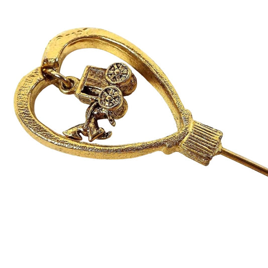 Enlarged top view of the retro vintage horse and carriage stick pin. The metal is gold tone in color. There is a large open heart at the top with a small dangling charm of a horse and buggy on the inside. 