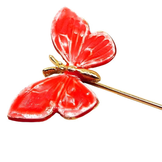 Magnified view of the top part of the retro vintage enameled butterfly stick pin. The metal is gold tone in color. The butterfly is a bright coral pink in color with a gold tone body. 