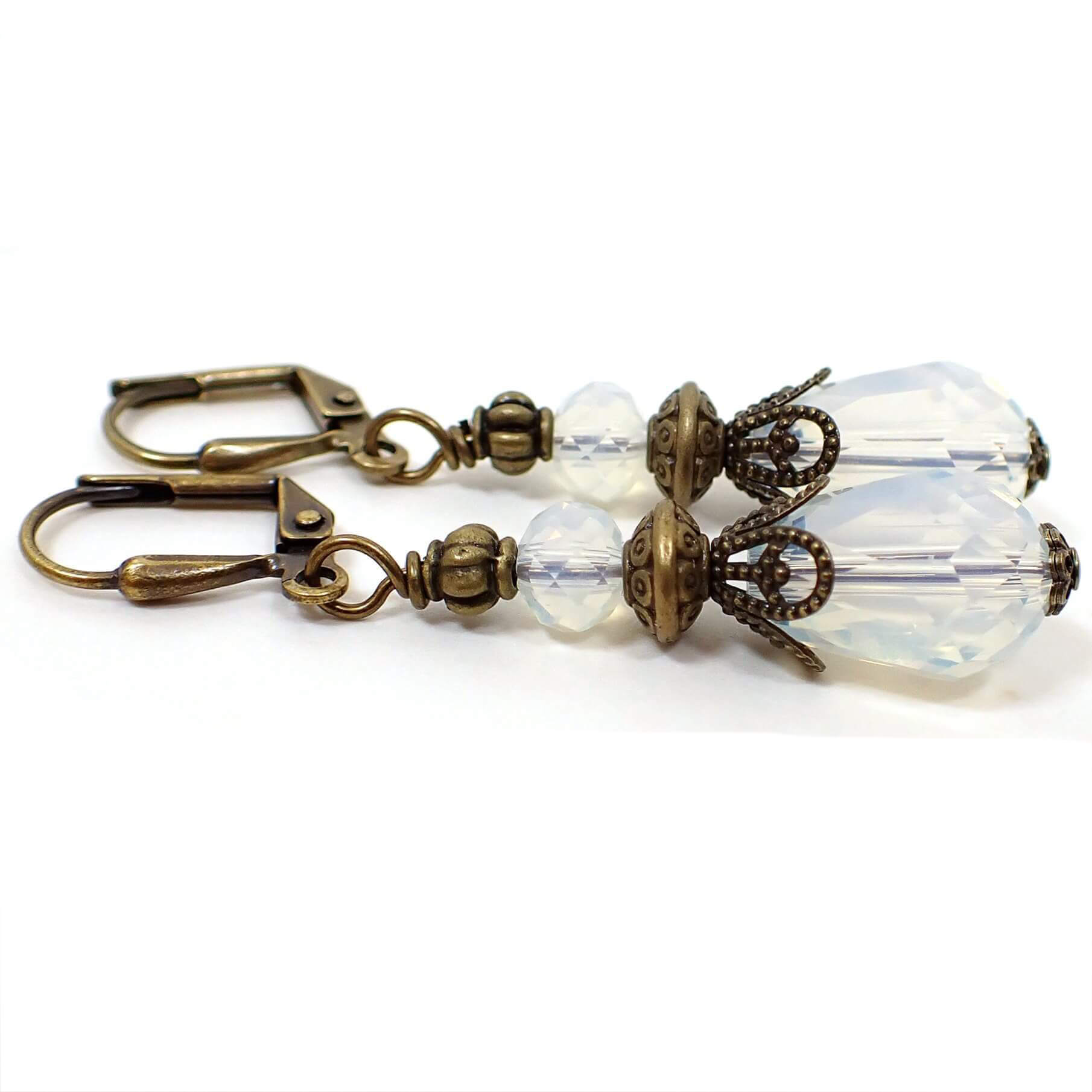 Side view of the handmade faceted glass crystal teardrop earrings. The metal is antiqued brass in color. The beads are translucent with a slightly cloudy opal color appearance.