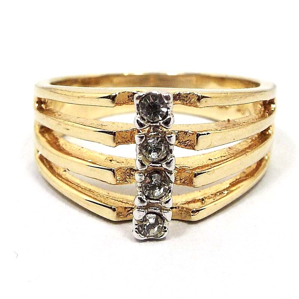 Front view of the retro vintage rhinestone ring. The metal is gold tone in color. The band is split at the sides and top into four band sections. Each one has a small prong set round rhinestone in the middle. 