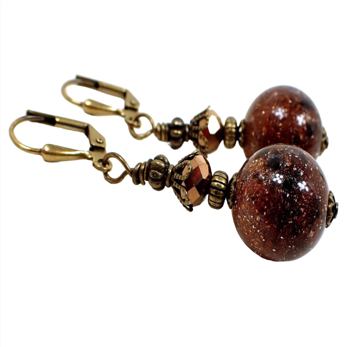 Angled side view of the handmade sparkly brown lucite galaxy earrings. The metal is antiqued brass in color. It has a faceted glass metallic brown bead at the top and a round lucite bead at the bottom that has tiny sparkles and swirls of brown and black that resembles a galaxy like appearance.