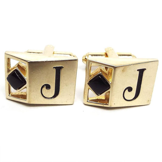 Front view of the retro vintage initial cufflinks. They are gold tone in color and have an angled out front. On the left side is a diamond shaped black glass cab. On the right is an engraved black letter J.