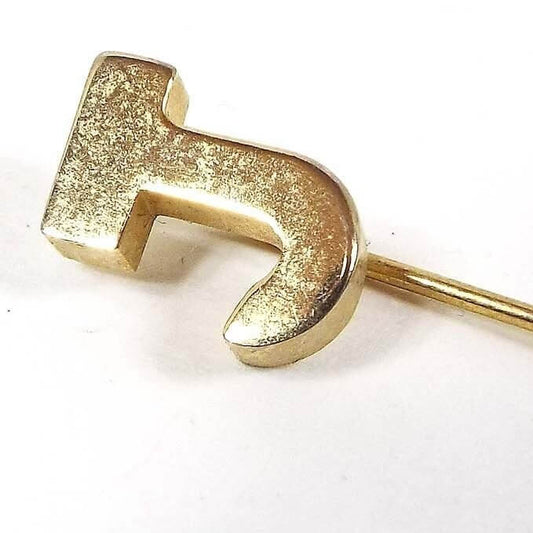 Enlarged view of the top of the Mid Century vintage initial stick pin. The metal is gold tone in color and there is a block style letter J at the top.