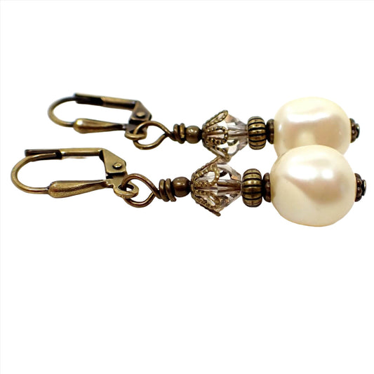 Side view of the handmade drop earrings with vintage lucite beads. The metal is antiqued brass in color and there are faceted glass crystals at the top. The bottom vintage beads are potato shaped and are pearly off white like faux pearls. 