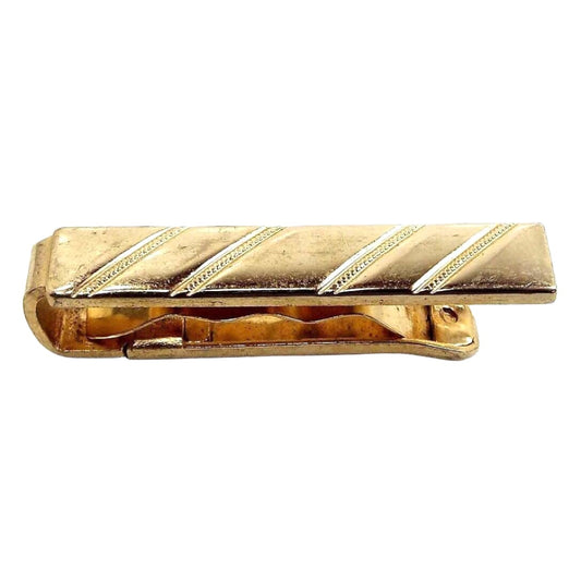 Angled top and side view of the Anson Mid Century vintage tie bar. The metal is gold tone in color. It is a slide on style tie bar that's smaller in size and has a wavy piece of metal in the middle of the front and back piece to help hold it in place on the tie. The front has a stamped diagonal stripe design.