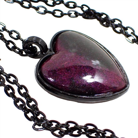 Enlarged front view of the handmade resin Goth heart pendant necklace. The chain and setting are black in color. The heart has a domed resin front with pearly dark pink and black resin. Some areas of the pink have hints of purple color depending on how the light hits it.