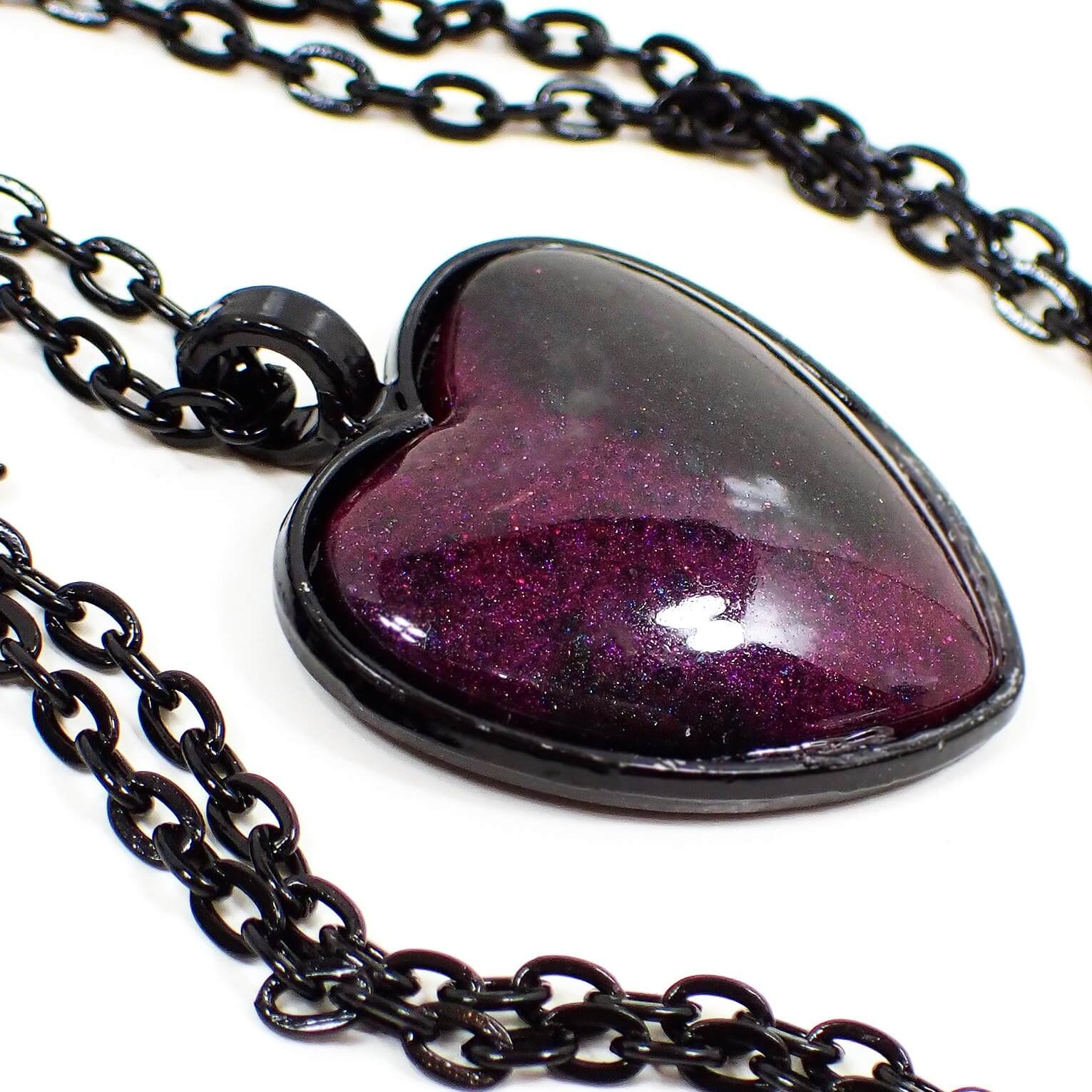 Enlarged front view of the handmade resin Goth heart pendant necklace. The chain and setting are black in color. The heart has a domed resin front with pearly dark pink and black resin. Some areas of the pink have hints of purple color depending on how the light hits it.