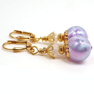 Side view of the pearly purple handmade earrings. The metal is gold plated in color. There are new faceted pearly white glass beads on the top. The bottom beads are round vintage plastic beads that have a swirled pearly AB purple appearance. There are pearly color shifts as you move around in the light.