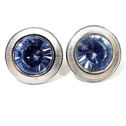 Front view of the Mid Century vintage round blue rhinestone cufflinks. The metal is silver tone in color. There are large blue rhinestones in the middle surrounded by a silver tone line textured edge. 