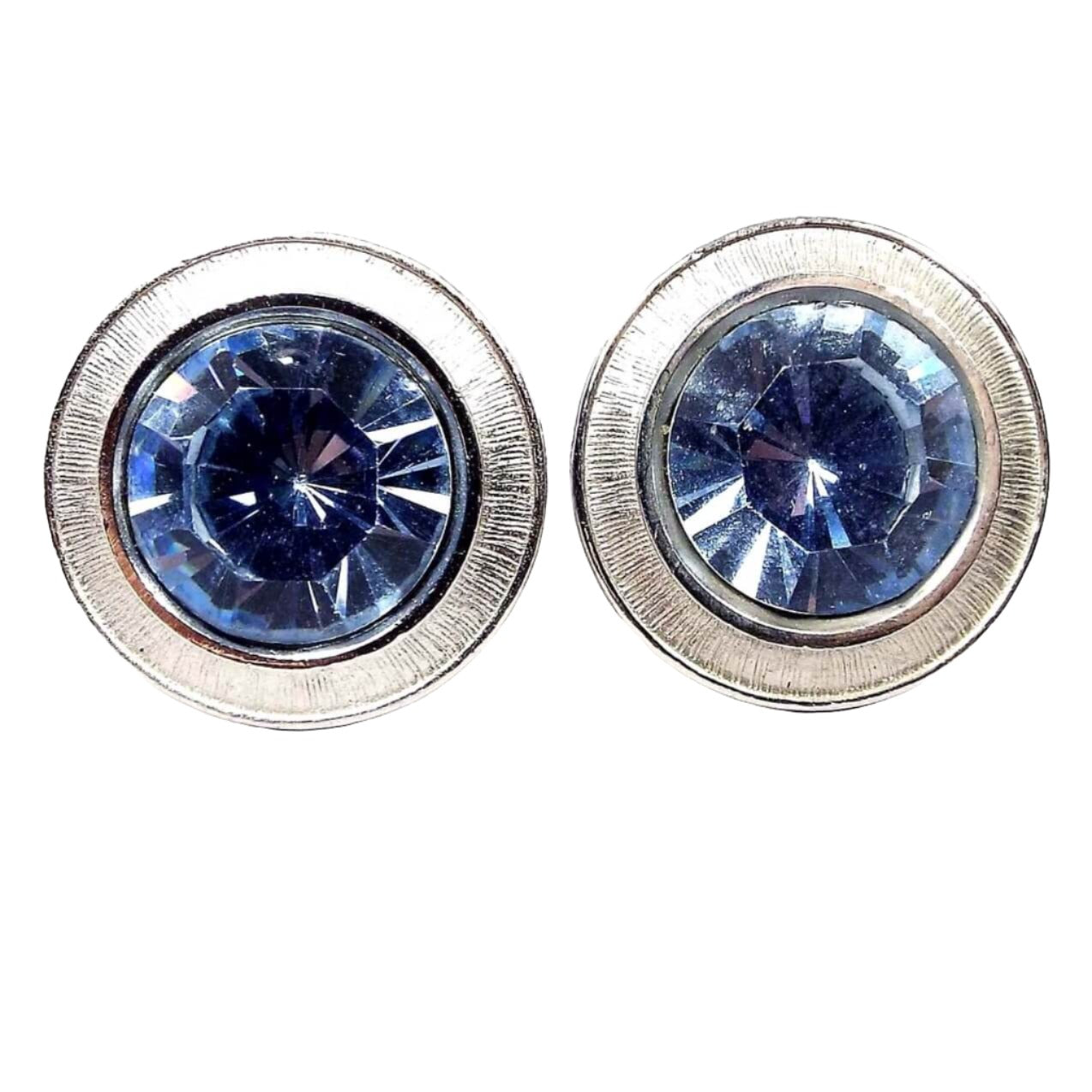 Front view of the Mid Century vintage round blue rhinestone cufflinks. The metal is silver tone in color. There are large blue rhinestones in the middle surrounded by a silver tone line textured edge. 
