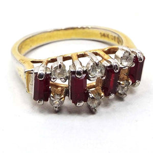 Front view of the retro vintage rhinestone cocktail ring. The metal is gold tone in color with some rub wear on the band showing the silver tone underneath. There are four rectangle baguette dark red rhinestones on the top with two small round clear rhinestones in between each red one at the top and bottom. All stones are prong set.
