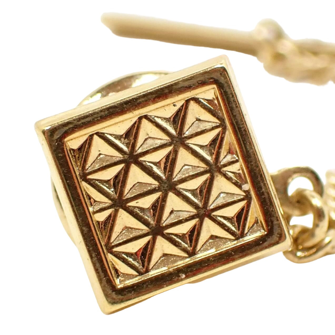 Enlarged front view of the retro vintage geometric tie tack. It is square shaped with gold tone plated color metal. There is a raised triangle pattern all across the front.