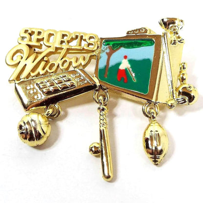 Front view of the retro vintage Danecraft enameled brooch pin. The metal is gold tone in color. It has Sports Widow at the top with cut out style lettering. There is a TV remote, basketball, ball and bat, football, bowling ball and pin, trophy, and TV as part of the brooch. Three of them are charms that dangle below. The TV part has enameling with a depiction of someone playing golf on it.