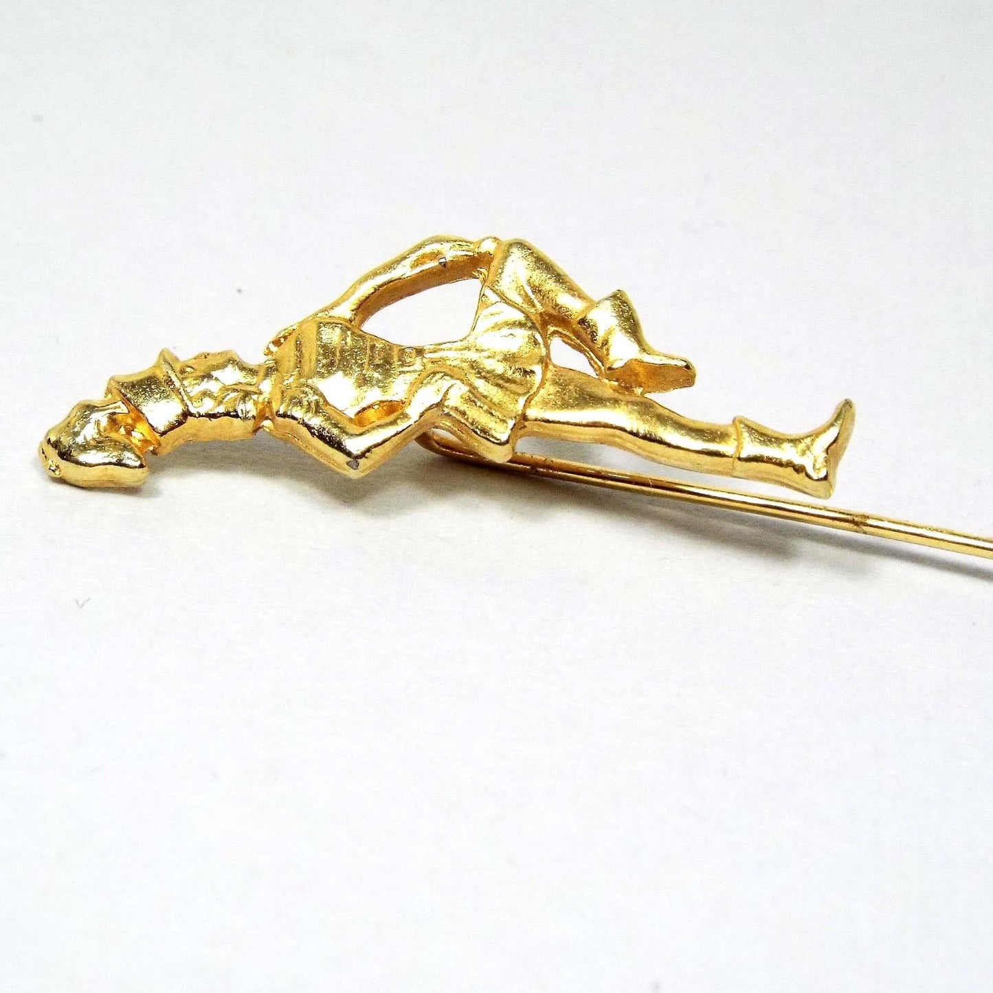 Enlarged top view of the Mid Century vintage marching band stick pin. The metal is gold tone in color. There is a girl in a marching band outfit holding a baton at the top.