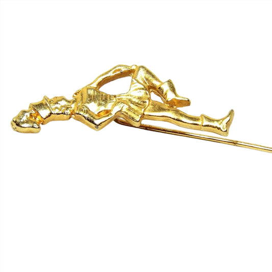 Enlarged top view of the Mid Century vintage marching band stick pin. The metal is gold tone in color. There is a girl in a marching band outfit holding a baton at the top.