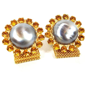 Front view of the Mid Century vintage rhinestone and faux pearl wrap around cufflinks. The metal is gold tone in color. There is a large round gray blue faux pearl cab in the middle surrounded by small orange rhinestones. There is a wide mesh chain coming from the bottom that goes around to the back.