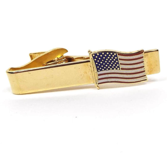 Front view of the retro vintage enameled American flag tie clip. The metal is gold tone in color. There is an enameled US flag at the end in red, white, and blue.
