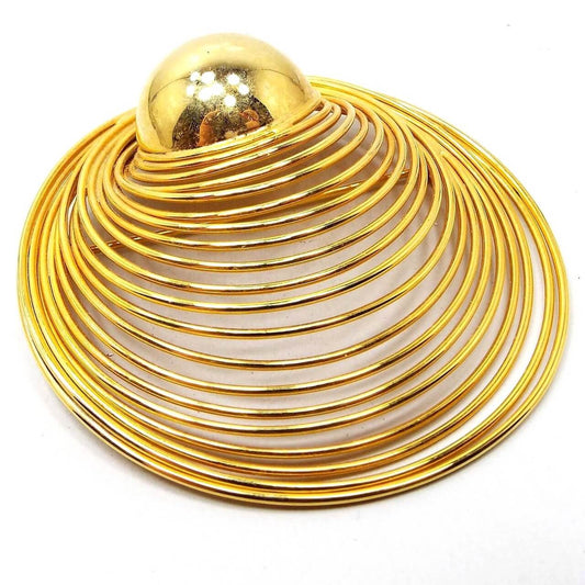 Angled view of the retro vintage wire brooch pin. It is gold tone in color. There is a domed round metal center with curved round wires angled out to one side.