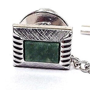 Front view of the retro vintage gemstone tie tack. It's silver tone in color and rectangle in shape. It has a Modernist style design with textured top and bottom and etched facets on the sides. There is a rectangle green moss agate cab in the middle.